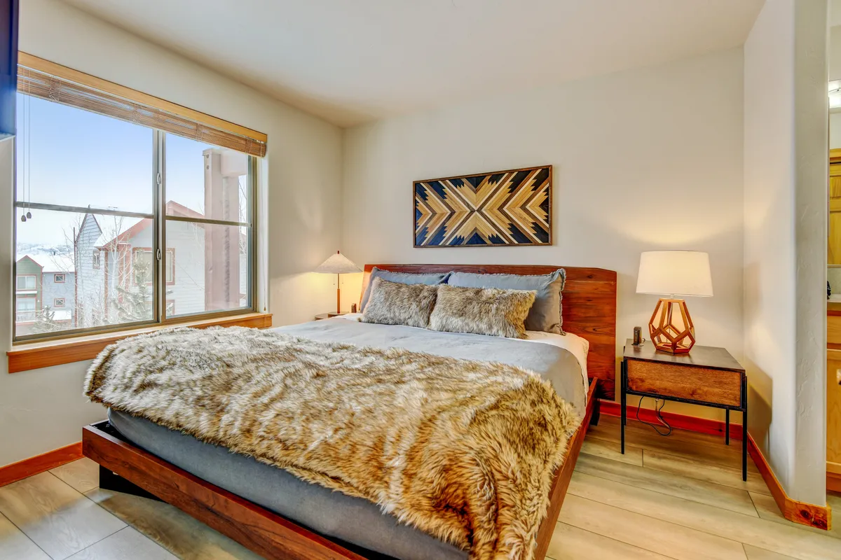 A cozy bedroom with a plush bed, decorative wall art, a nightstand with a lamp, and sunlight streaming through the window. The ambiance is serene and soothing, ideal for unwinding after a day of adventure.