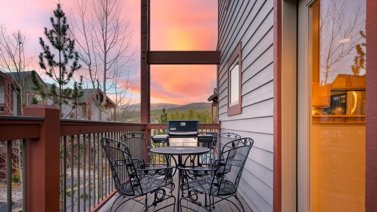 An inviting outdoor dining table is set on a deck with mountain views and a colorful sunset sky. The area is perfect for meals, gatherings, and stargazing, with plenty of space for both people and pets to relax outdoors.