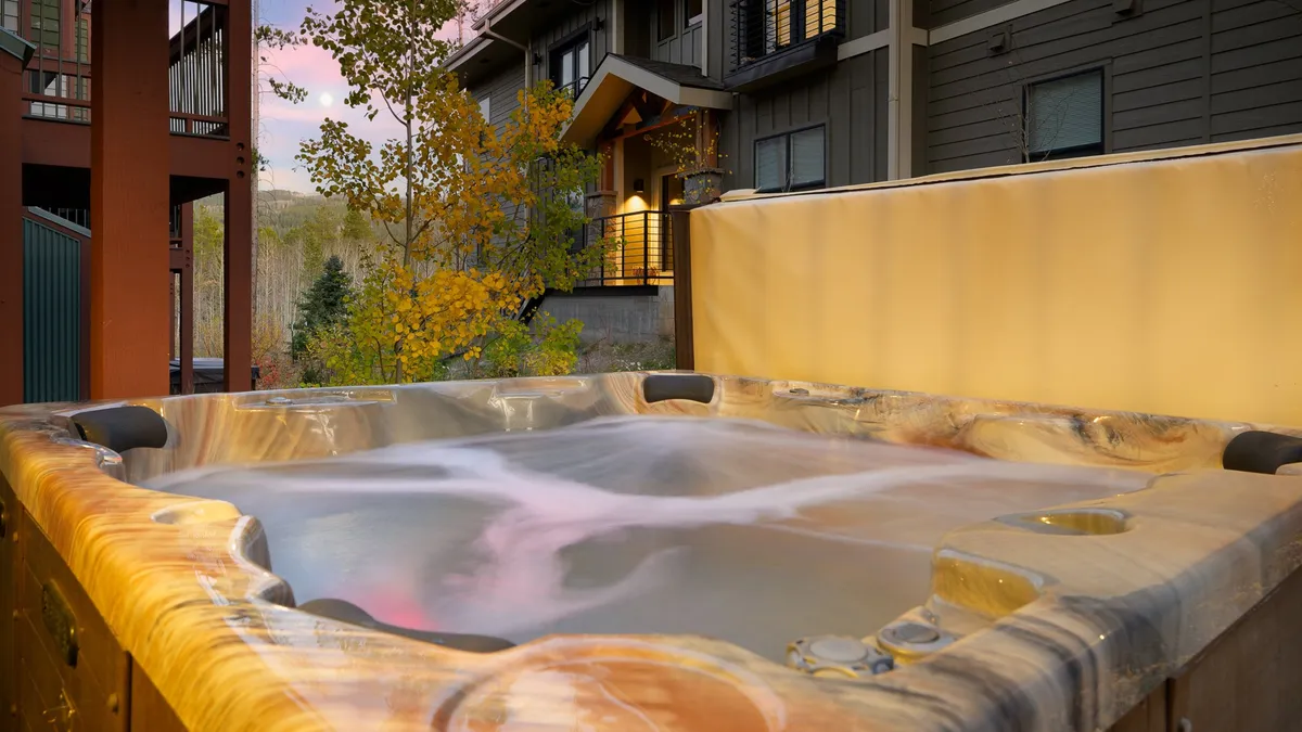 This exterior image features a bubbling hot tub nestled amid surrounding trees, with the building facade visible. The scene conveys a tranquil mood, ideal for relaxing and soaking while taking in nature.