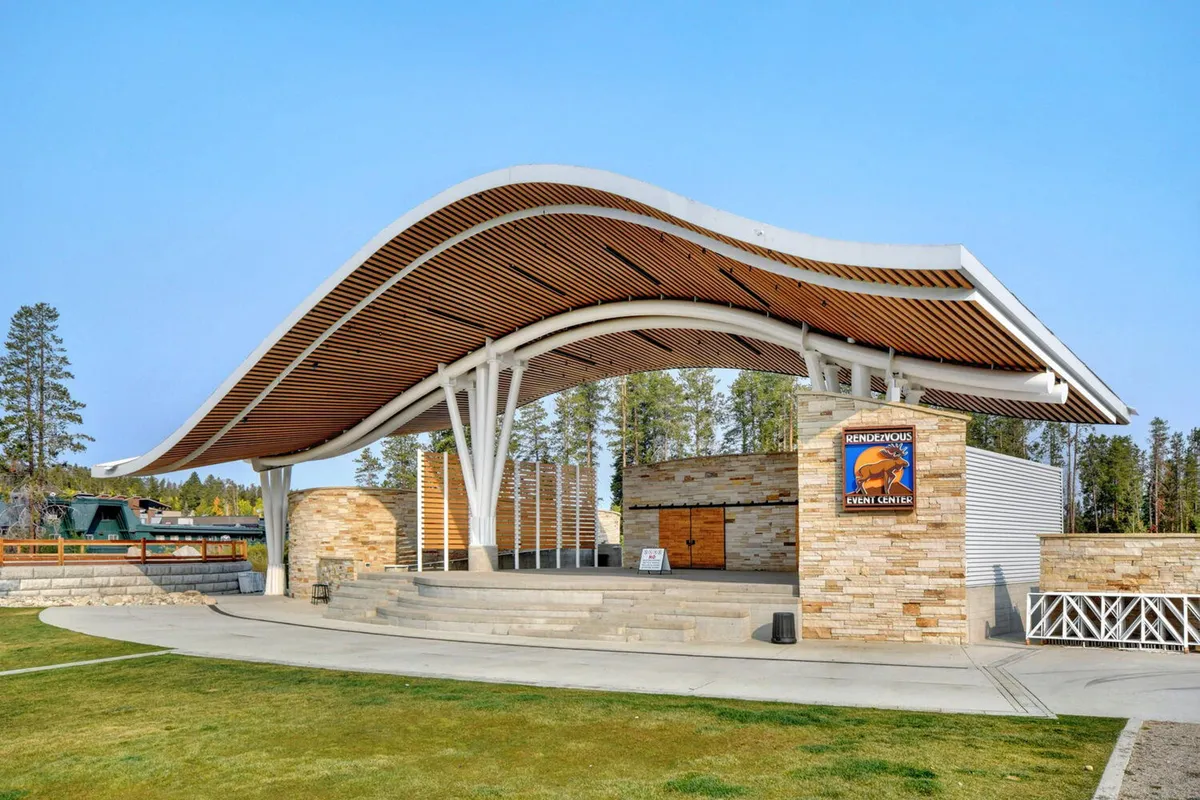 An inviting exterior shot of Hideaway Park's outdoor amphitheater, featuring its distinctive wave-like roof, stone and wood architectural elements, and visible signage. The scene hints at the amphitheater’s role as a vibrant hub for community events and outdoor performances, set against the natural backdrop of Winter Park.