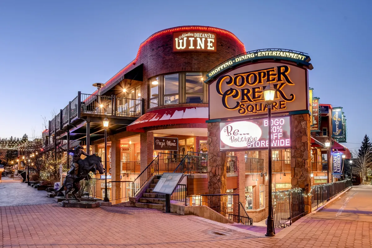 A vibrant streetscape at Cooper Creek Square, showcasing the entrance to a wine store, inviting outdoor seating, and decorative lighting, exuding energy and sophistication.