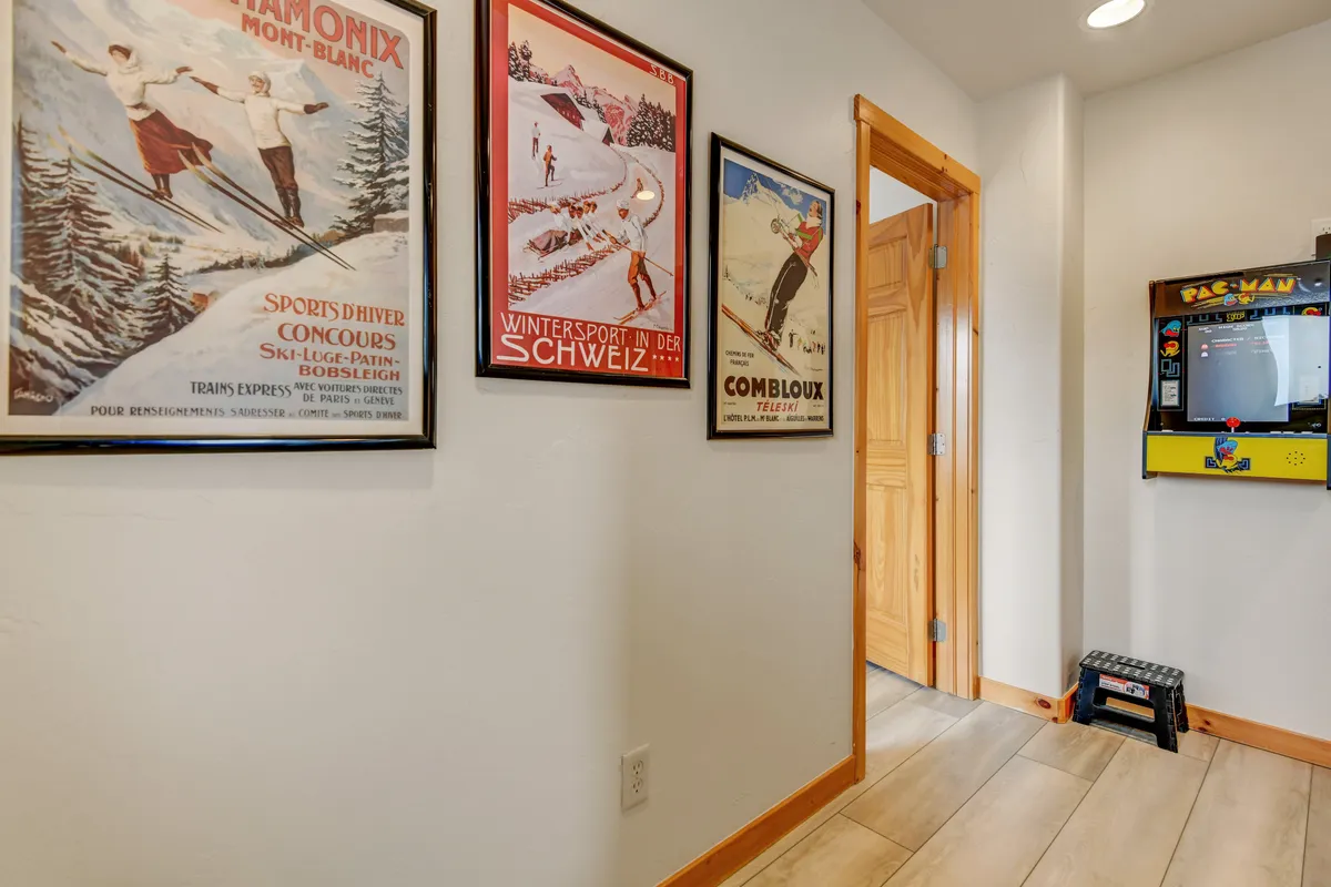 The scene captures a cozy corner with a vintage arcade game machine and vintage ski posters on the wall. The wooden framing and soft lighting evoke a warm, playful, and inviting mood, emphasizing both the entertainment and retro design elements of the loft.