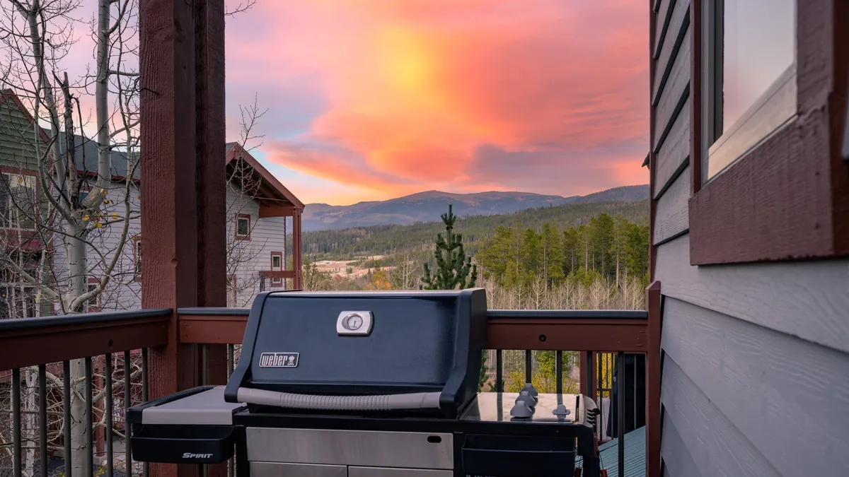 A sleek gas grill is positioned on an outdoor deck with expansive mountain views and a colorful sky, inviting guests to barbecue, dine, and stargaze in a relaxed atmosphere.