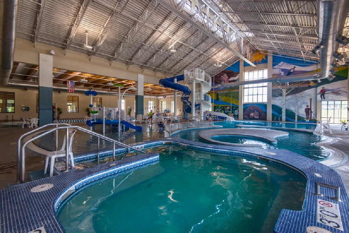 This vibrant interior image captures children playing on a water slide, with pool areas and a colorful mural in the background. The joyful atmosphere evokes memories of family vacations and highlights amenities like pools and water play that appeal to all ages.