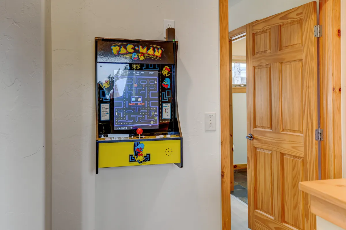 The image focuses on a classic Pac-Man arcade machine, set in a cozy corner with a wooden door frame. The arcade is warmly lit, inviting families to gather for friendly competitions and shared laughter.