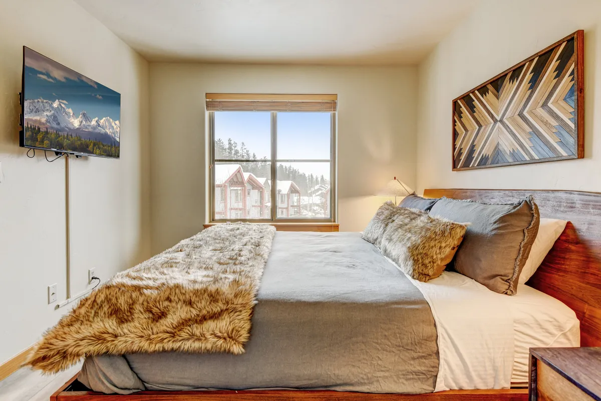 A tranquil bedroom featuring a plush bed with premium bedding, artwork on the walls, a large window offering scenic views, and a television set for relaxing evenings. The soft, inviting lighting and serene decor make the space feel like a private retreat.