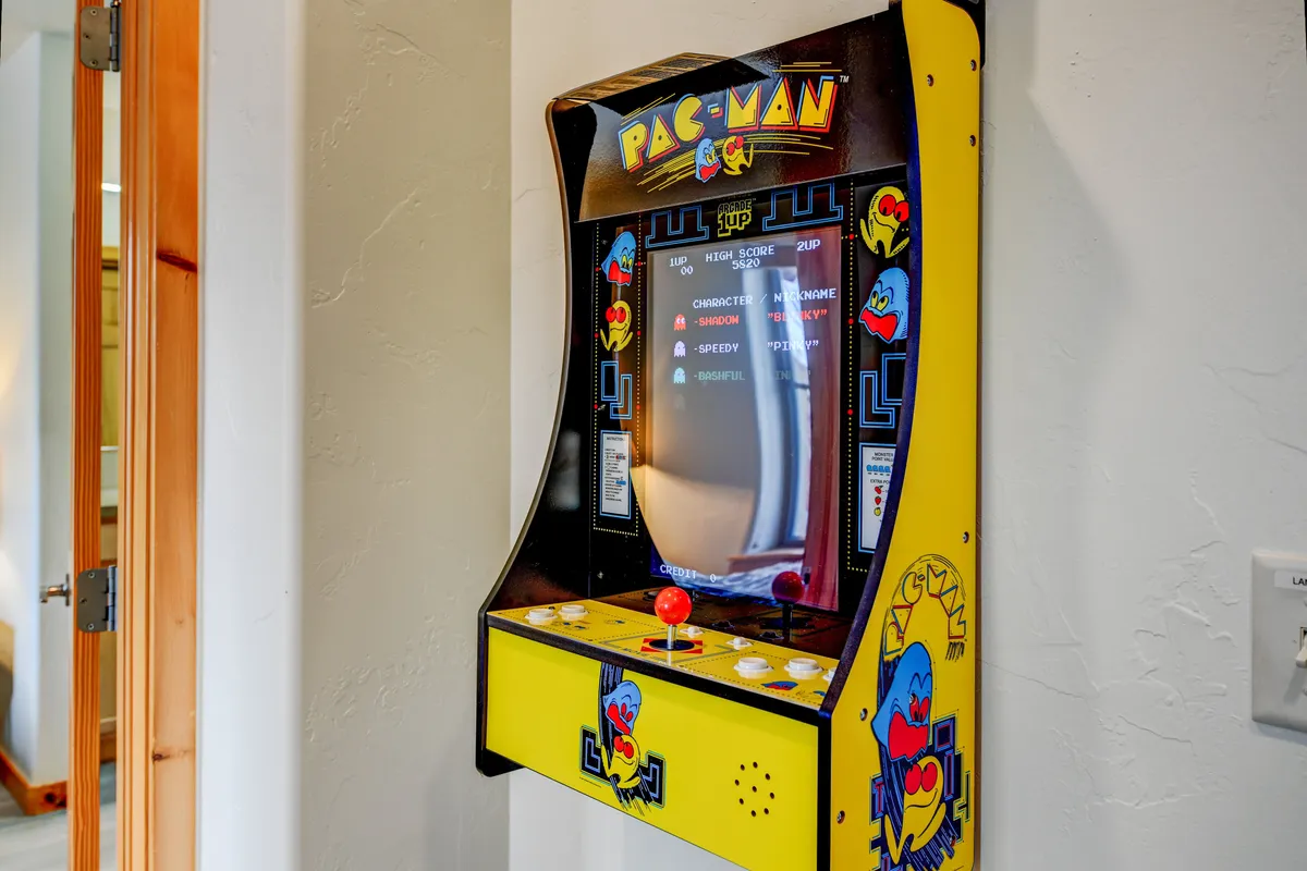 This image centers on a Pac-Man arcade machine set in a bright, inviting loft space. The nostalgic vibe is enhanced by the focus on the arcade game, with subtle hints of comfortable seating and a playful atmosphere in the background, suggesting a fun, interactive area for guests of all ages.