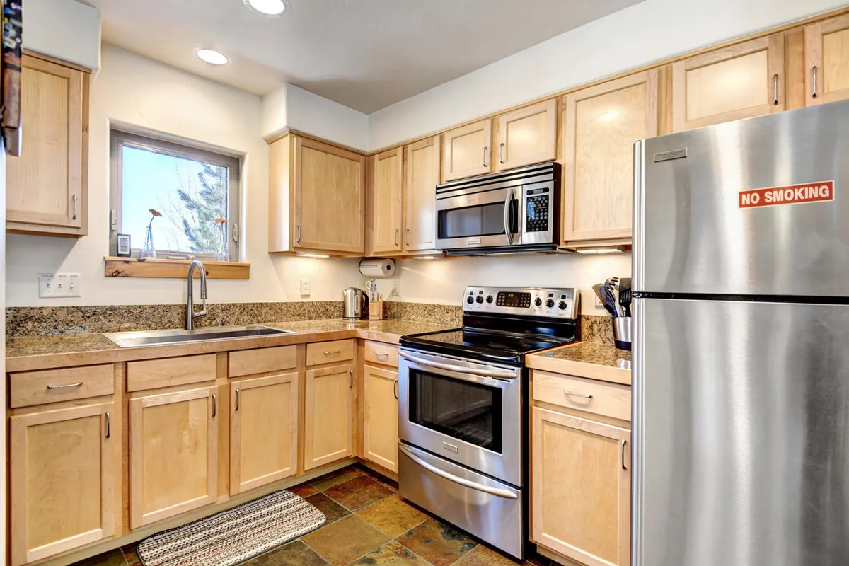 A well-appointed kitchen featuring stainless steel appliances, granite countertops, and warm wooden cabinetry. There's a window over the sink offering natural light and a glimpse outside, and the countertops are spacious, perfect for meal prep or gathering around. The setting suggests both practicality and a sense of cozy, family-oriented activity.