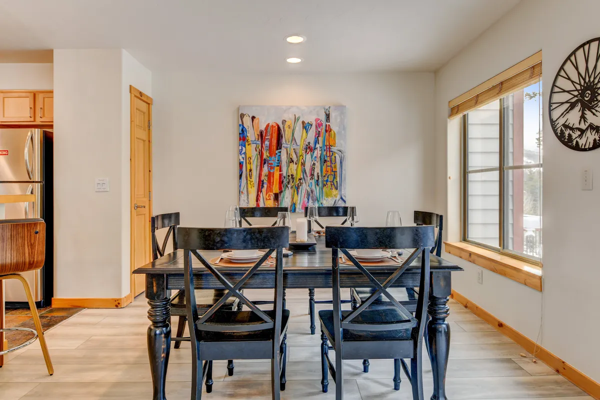 A vibrant dining area with a large wooden table, colorful artwork on the walls, and a bright window that lets in natural light. The setting is lively and welcoming, with enough space for family meals or gatherings with friends, and the backdrop of the mountains visible through the window.