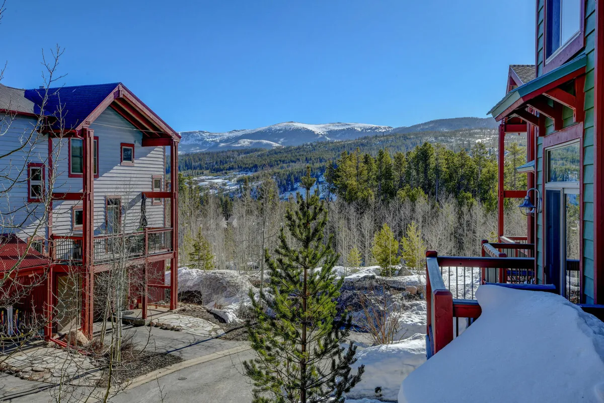 A serene exterior view featuring a sweeping mountain landscape, colorful lodge-style buildings, and tall pine trees. The open outdoor space hints at walking paths and direct access to nature, making it ideal for guests seeking adventure and time with their pets.