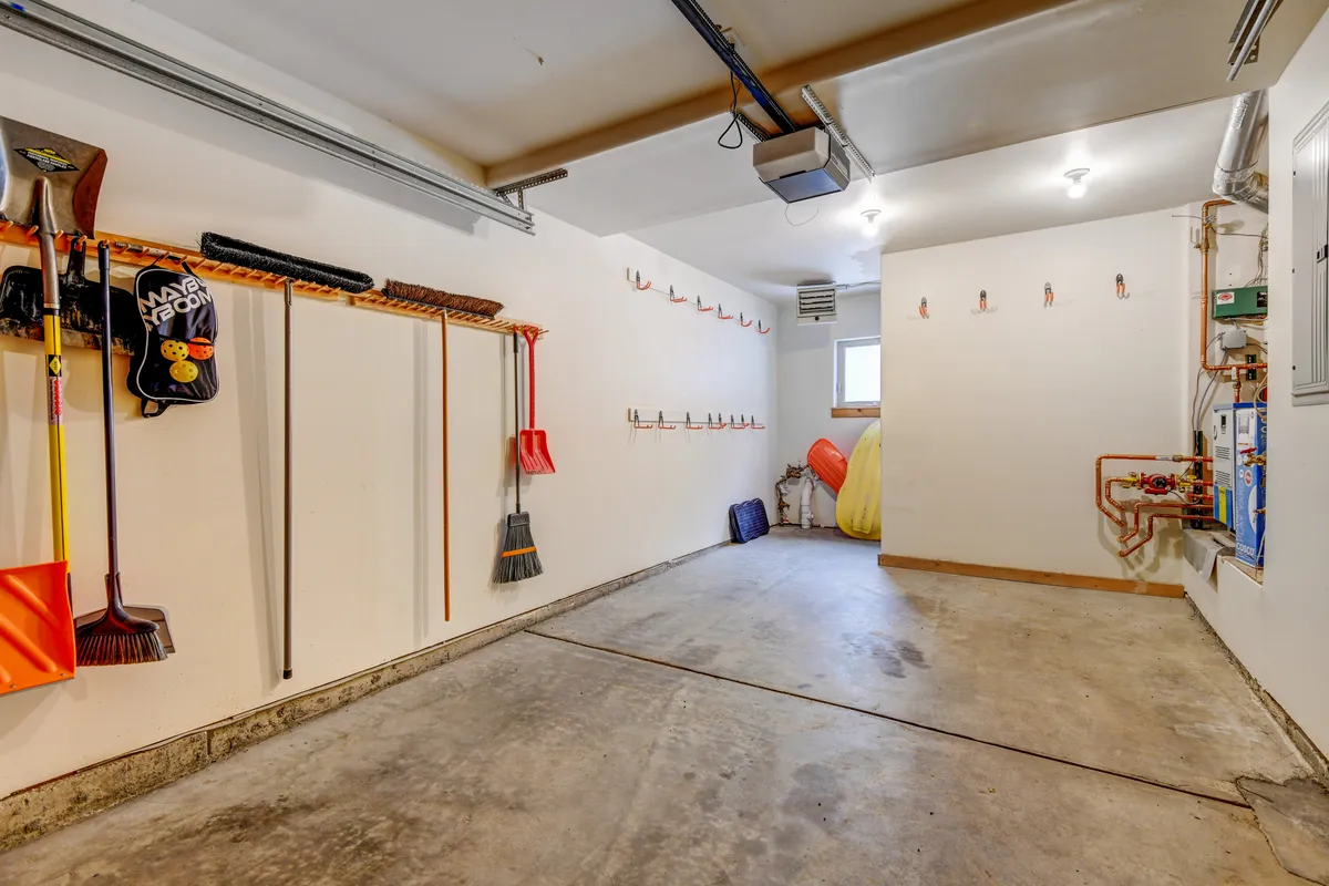 An organized garage with tool storage and space for parking, featuring a clean concrete floor and brightly colored equipment. The area is tidy and functional, ideal for secure vehicle and bike storage.
