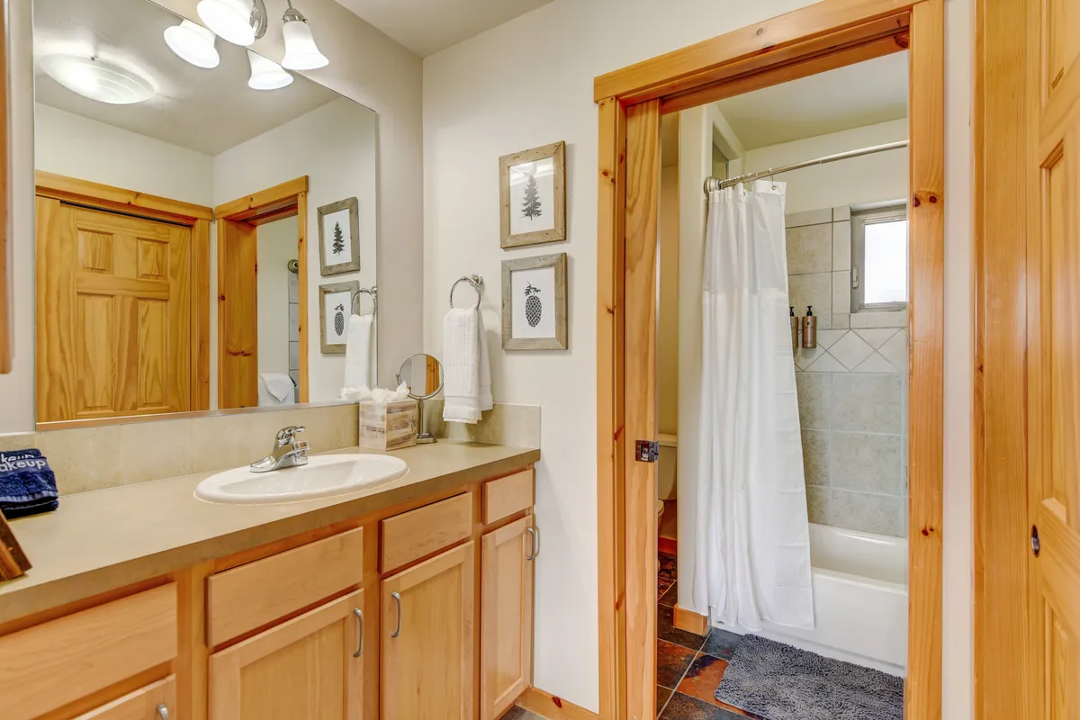 A spa-inspired bathroom with a sleek vanity, wooden cabinetry, framed artwork, and a shower area. The space feels fresh and calming, reflecting luxury amenities and organic bath products.