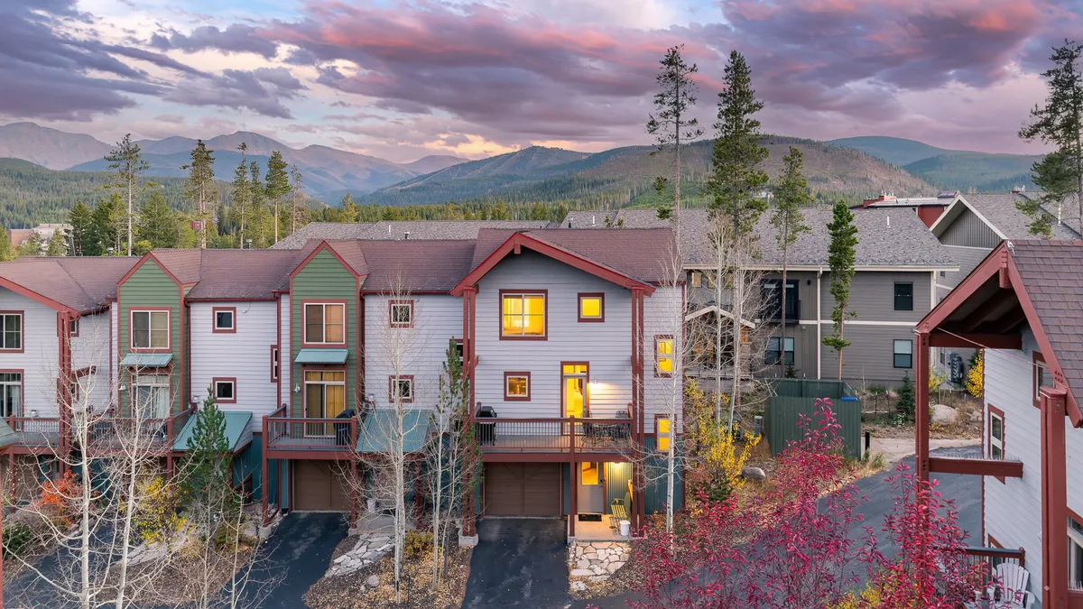 A picturesque exterior landscape with a mountain backdrop, lush greenery, and a vivid sunset sky. Well-maintained buildings border open areas, hinting at opportunities for evening strolls and outdoor fun.